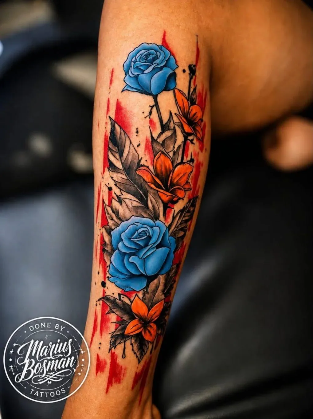Forearm tattoo of blue roses and orange lilies with red brush-stroke background