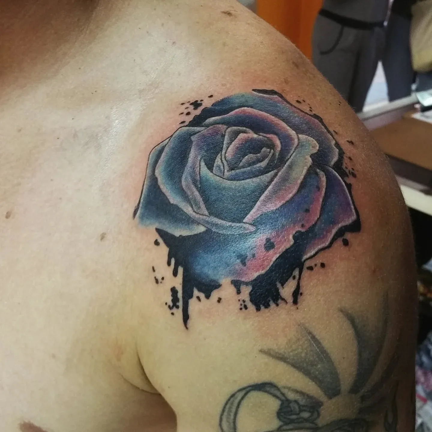 Blue and pink watercolour-style rose with black ink splatter on a shoulder